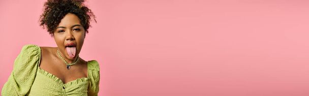 Elegante mujer afroamericana sobresaliendo lengua sobre fondo rosa. - Foto, Imagen