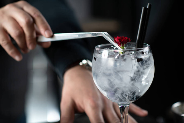 Barkeeper fügt eine zarte essbare rote Blume hinzu, die den Charme des Gin Tonic Cocktails unterstreicht. - Foto, Bild