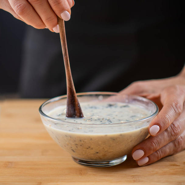 mujer preparando harina de avena con avena, leche de soja y proteína vegetal en polvo, mostrando la fusión de salud y sabor - Foto, imagen