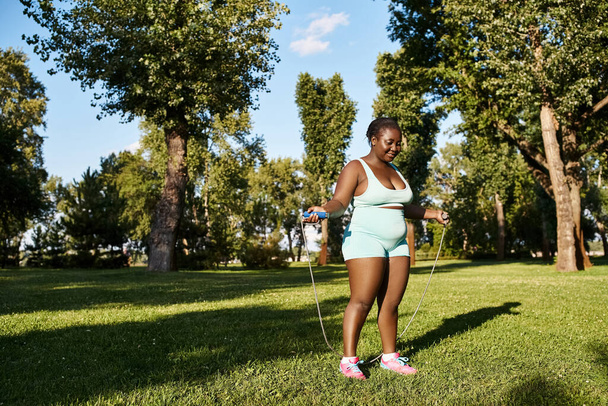 Una donna afroamericana in abbigliamento sportivo esplora il suo potenziale corporeo, brandendo con grazia una corda che salta all'aperto.. - Foto, immagini