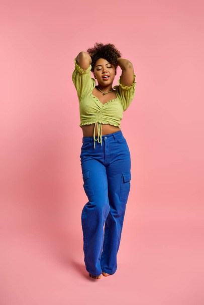 Κομψό Αφρο-Αμερικανίδα ποζάρει σε κίτρινο top και μπλε παντελόνι με φόντο ζωντανό. - Φωτογραφία, εικόνα