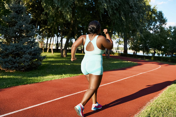 Afroamerykanka w odzieży sportowej biegnie po czerwonym torze, pokazując pozytywność i atletyzm ciała.. - Zdjęcie, obraz
