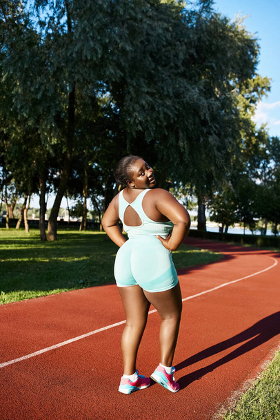 Egy afro-amerikai nő sportruházatban magabiztosan áll egy teniszpályán, kezével a csípőjén.. - Fotó, kép