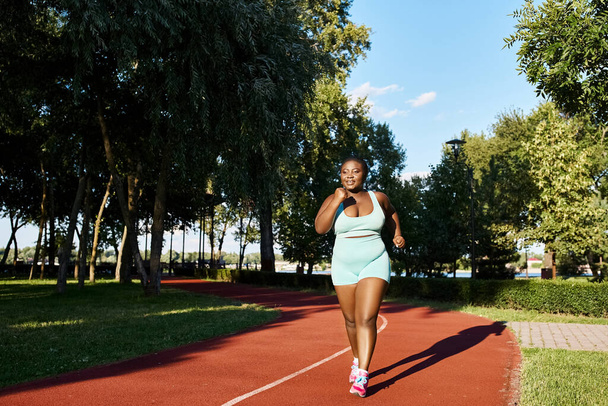Zakrzywiona Afroamerykanka w sportowej odzieży biegnie po czerwonym torze. - Zdjęcie, obraz