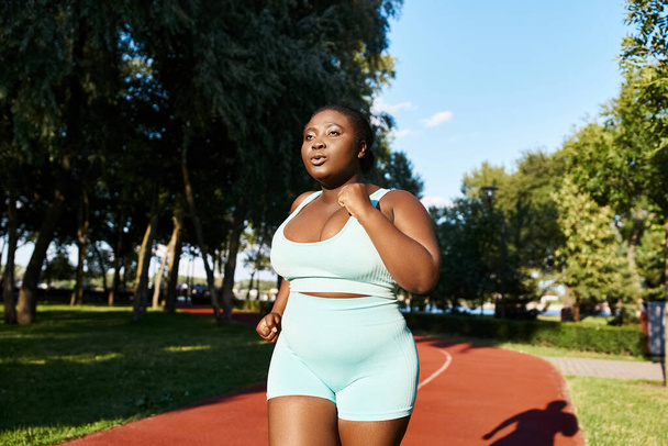 Zakrzywiona Afroamerykanka pewnie ćwiczy na świeżym powietrzu w niebieskim sportowym staniku i spodenkach. - Zdjęcie, obraz