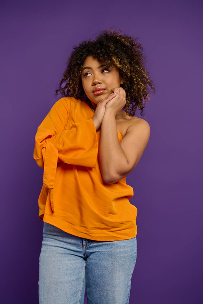 Emocional mujer afroamericana en camisa naranja con estilo golpea una pose contra un telón de fondo vibrante. - Foto, Imagen