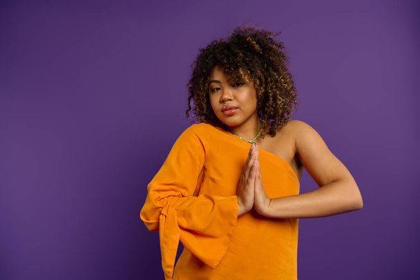 Stylish African American woman posing in orange top against vibrant purple backdrop. - Photo, Image