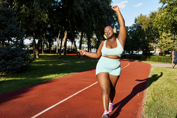 Een Afro-Amerikaanse vrouw in sportkleding loopt vol vertrouwen over een rode baan buiten, die lichaamspositiviteit en kracht belichaamt. - Foto, afbeelding