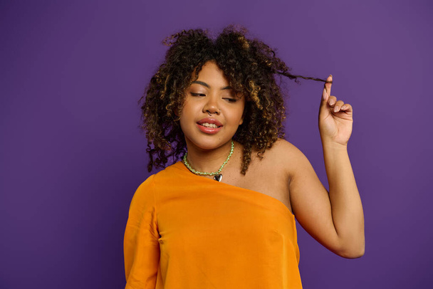 Стильная афроамериканка в оранжевом топе расчесывает волосы. - Фото, изображение