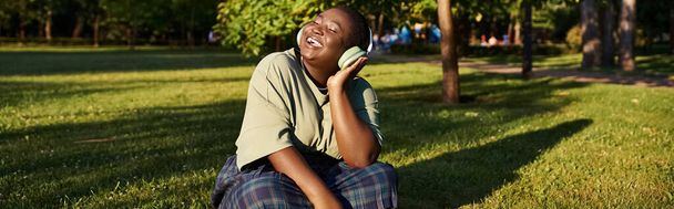 czarna kobieta siedzi w bujnej trawie, ciesząc się spokojem na świeżym powietrzu w słoneczny dzień. - Zdjęcie, obraz