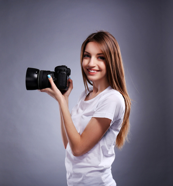 Young female photographer taking photos on grey background - 写真・画像