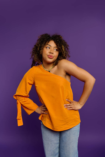 Een mooie Afro-Amerikaanse vrouw met emotionele expressie poseert stijlvol in een oranje top tegen een levendige achtergrond. - Foto, afbeelding