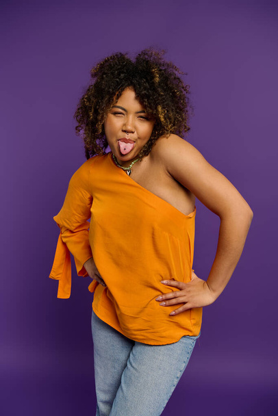 Elegante mujer afroamericana juguetonamente posa con la lengua hacia fuera contra el telón de fondo vibrante. - Foto, imagen