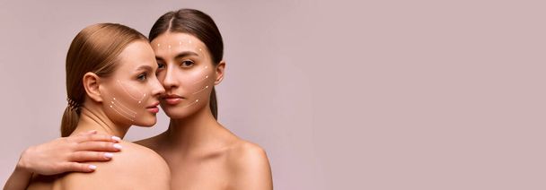 Banner. Two beautiful women with lifting arrows showing facial anti-aging treatment on skin against grey studio background. Negative space. Concept of beauty procedures, cosmetology treatment, massage - Photo, Image