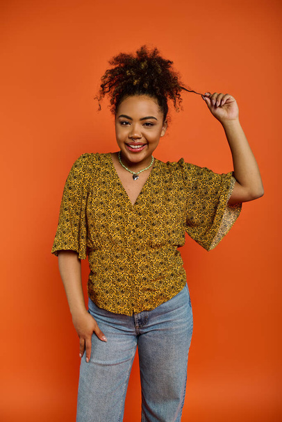 Афроамериканка в стильной одежде позирует на ярком оранжевом фоне. - Фото, изображение