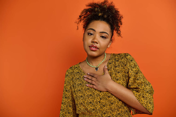 A stylish African American woman posing in front of a vibrant orange backdrop wearing a statement necklace. - Photo, Image