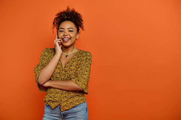 Улыбающаяся афроамериканка в стильной одежде разговаривает по мобильному телефону на ярком фоне. - Фото, изображение