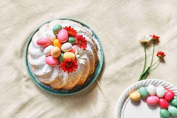 Πασχαλινό κέικ διακοσμημένο με άχνη ζάχαρη, μικρά πολύχρωμα σοκολατένια αυγά και μαργαρίτα λουλούδια. Παραδοσιακό πασχαλινό κέικ ή γλυκό ψωμί με επικάλυψη. Πασχαλινό. - Φωτογραφία, εικόνα