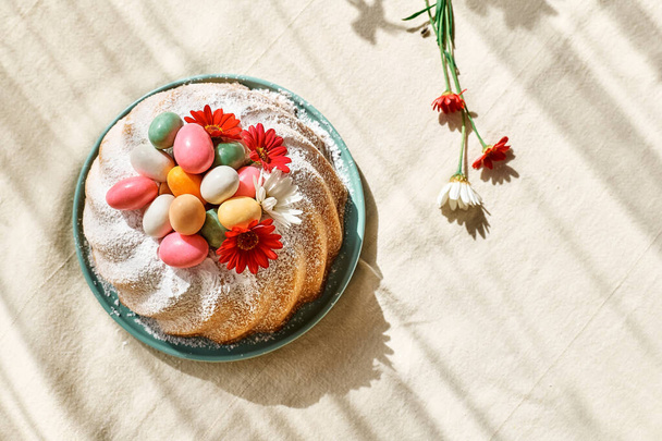 Pääsiäiskakku koristeltu kuorrutussokerilla, pienillä värikkäillä suklaamunilla ja päivänkakkaroilla. Perinteinen pääsiäiskakku tai makea leipä keveällä. Pääsiäislahja. - Valokuva, kuva