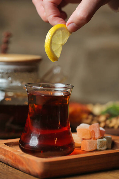A person dips a lemon into a glass filled with tea. - Photo, Image