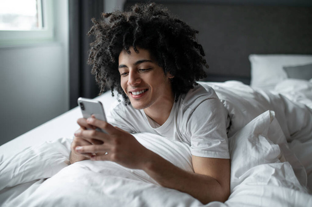 Chatting. Young man lying in bed and texting on his phone - Фото, зображення