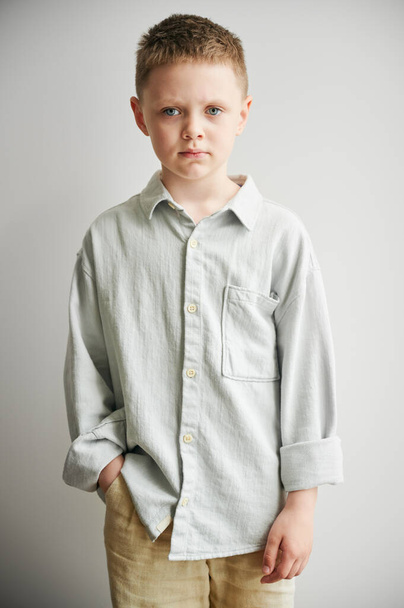 Portrait of young sad boy keeping hand in pocket, looking to the camera. Serious kid in casual clothes posing on white background. - Photo, Image