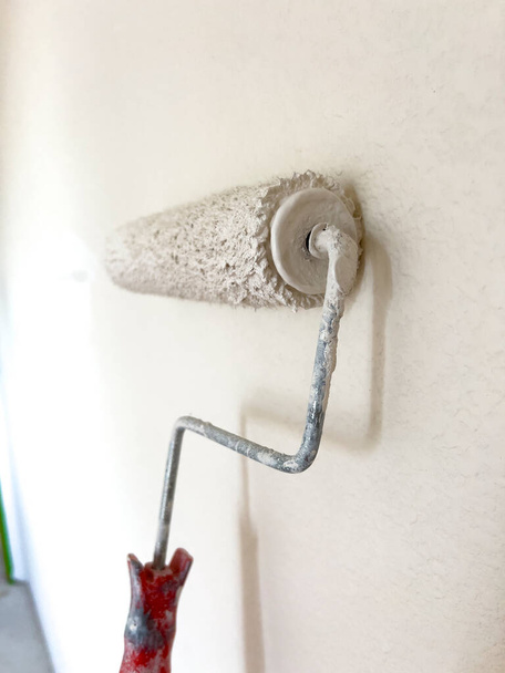 Detailed process of painting a wall, with a focus on a paint roller applying a fresh white coat, symbolizing the transformative power of a simple home improvement task. - Photo, Image