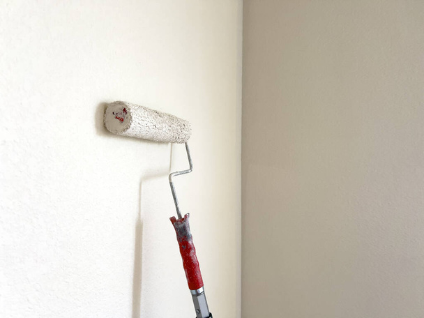 Processo detalhado de pintura de uma parede, com foco em um rolo de pintura aplicando um casaco branco fresco, simbolizando o poder transformador de uma tarefa simples de melhoria de casa. - Foto, Imagem