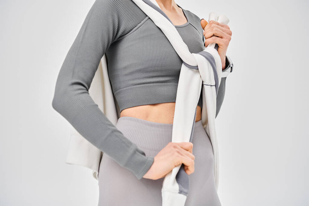 Een sportieve jonge vrouw poseert vol vertrouwen in haar grijze topje en legging tegen een grijze achtergrond. - Foto, afbeelding