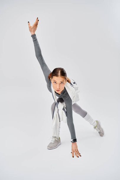 Una joven deportista en ropa activa bailando con gracia en un estudio sobre un fondo gris. - Foto, imagen