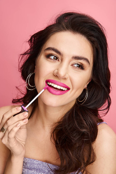 Una hermosa mujer con belleza natural exhibe lápiz labial rosa en sus labios contra un vibrante telón de fondo. - Foto, imagen