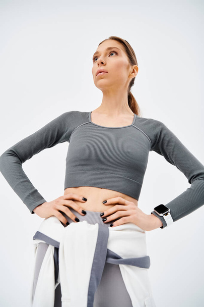 Sportovní mladá žena v aktivním oblečení sebevědomě stojí s rukama v bok na šedém pozadí. - Fotografie, Obrázek