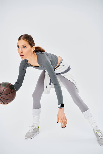 Een sportieve jonge vrouw houdt een basketbal voor een witte achtergrond. - Foto, afbeelding