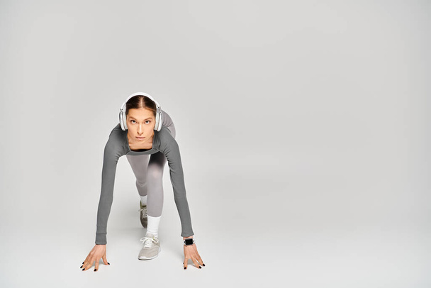 Una giovane donna sportiva in abbigliamento attivo mostra la sua forza eseguendo una spinta verso l'alto con le mani su uno sfondo grigio. - Foto, immagini