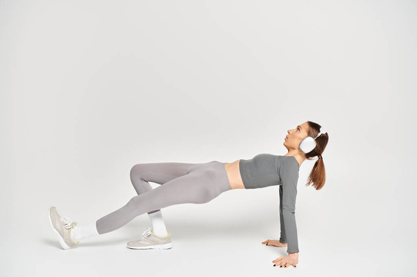 Una joven deportista realiza un ejercicio de tablón lateral con gracia y fuerza sobre un fondo blanco. - Foto, imagen