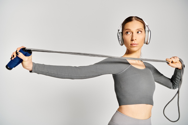 Sportliche junge Frau in aktiver Kleidung hält anmutig ein Springseil, das Kraft und Gleichgewicht verkörpert, mit Kopfhörer auf. - Foto, Bild