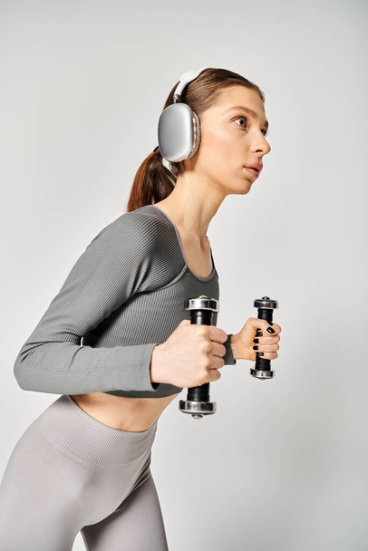 Femme sportive en tenue active tenant des haltères avec écouteurs allumés, prête pour une séance d'entraînement. - Photo, image