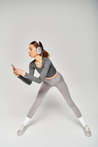 Eine sportliche junge Frau in grauer Aktivkleidung strahlt Zuversicht und Anmut aus, als sie sich auf einem neutralen grauen Hintergrund bewegt. - Foto, Bild
