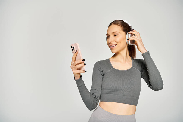Urheileva nuori nainen hoitaa vaivattomasti matkapuhelinta ja kuulokkeita.. - Valokuva, kuva