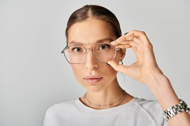 Genç bir kadın, gri bir arka planda kendine güvenen gözlük ve beyaz bir gömlek takıyor.. - Fotoğraf, Görsel