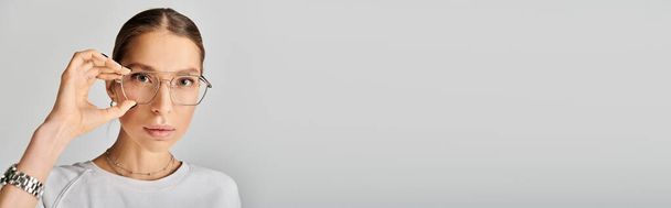 Молода жінка в білій сорочці і окулярах позує на сірому фоні, виключаючи почуття витонченості і інтелекту. - Фото, зображення