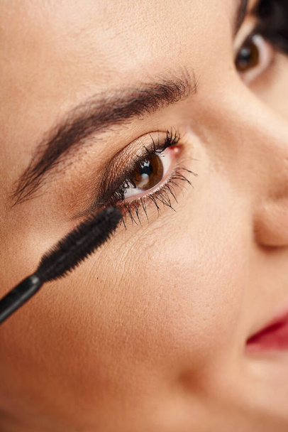 Gros plan portrait d'une jolie femme se maquillant avec un mascara près de l "œil. - Photo, image