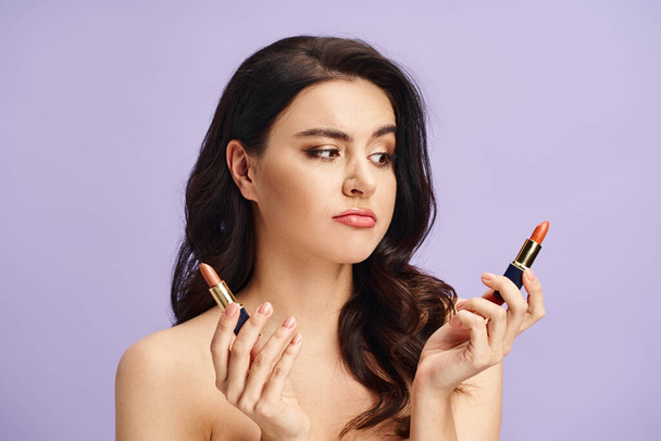 Una mujer con belleza natural sostiene dos lápices labiales vibrantes en sus manos. - Foto, imagen