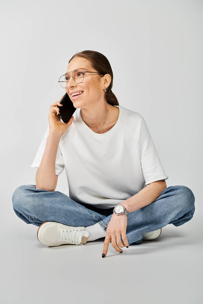 Una mujer con una camiseta blanca sentada en el suelo, ocupada en una llamada telefónica. - Foto, imagen