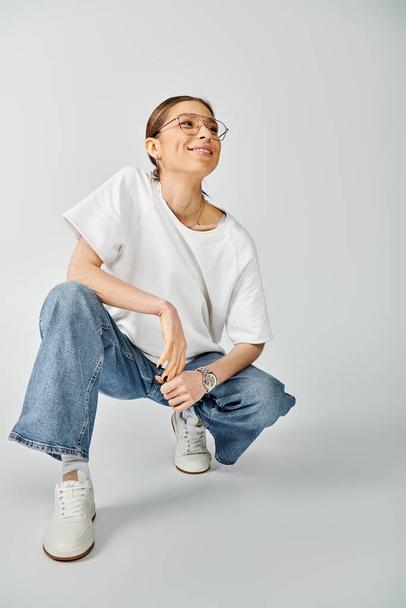A young woman in a white shirt and jeans striking a pose against a grey background. - Photo, Image