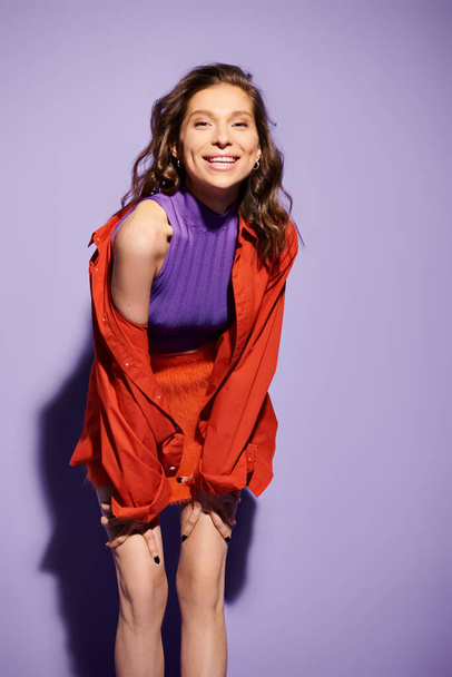 Una mujer joven con estilo exuda elegancia y confianza mientras posa para una imagen en un rojo vibrante sobre un fondo púrpura. - Foto, imagen