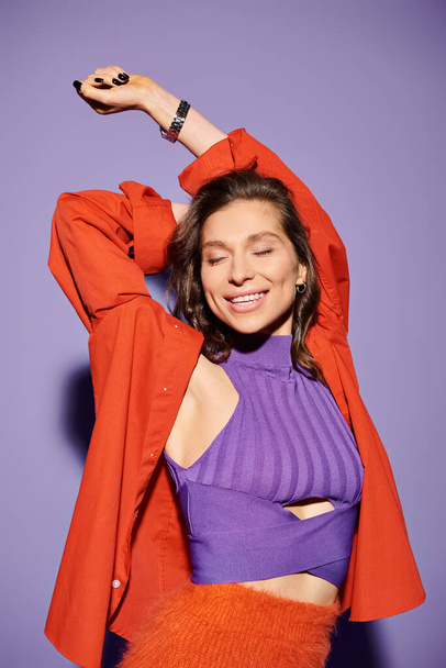 A stylish young woman wearing a purple top and an orange jacket against a purple background. - Photo, Image