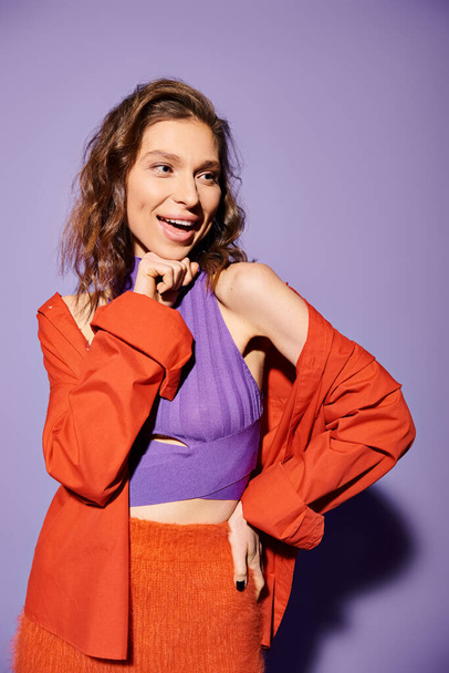 Stylish young woman exudes confidence in a purple top and an orange skirt against a vibrant purple background. - Photo, Image