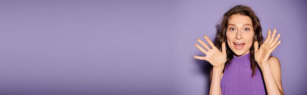 Стильна молода жінка в яскраво-фіолетовій сукні своїми руками прикриває обличчя на яскраво-фіолетовому тлі. - Фото, зображення