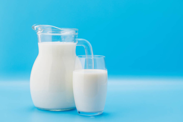 Свежее молоко в кувшине и стакане на синем фоне с копировальным пространством - Фото, изображение